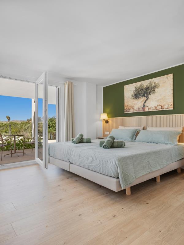 Slaapkamer 1 met tweepersoonsbed, groene accentwand en terrasdeuren met bergzicht