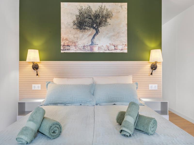 Bed in kamer 3 met olijfboomschilderij en opgerolde handdoeken